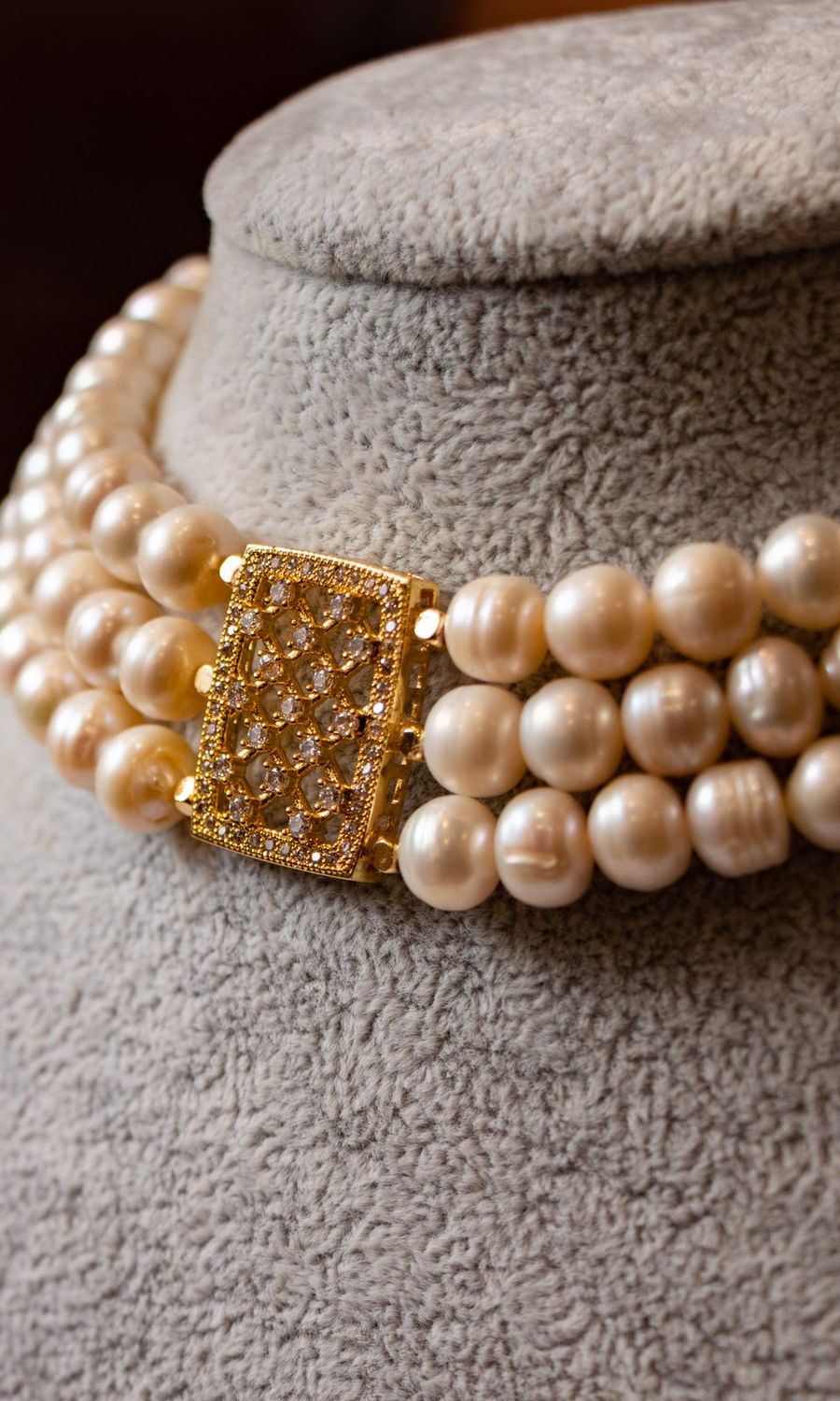 A three-strand pearl choker with a gold clasp on a jewellery bust